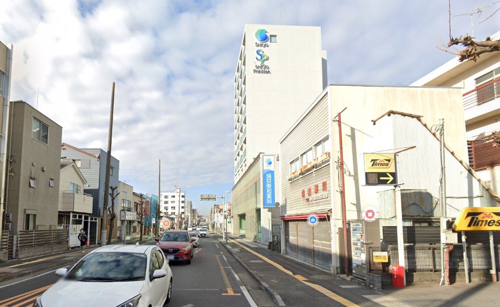 どでんを過ぎたあともまっすぐ続く道の写真。右手にタイムズ駐車場や白いビルが見える